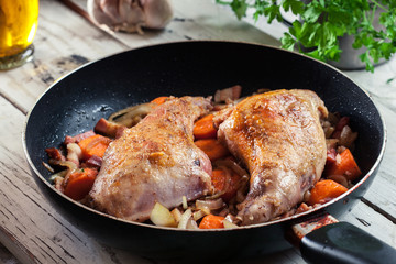 Fried rabbit legs on frying pan with vegetables