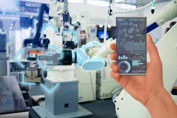 Engineer uses a futuristic transparent smartphone to control robots in a smart factory. Smart...