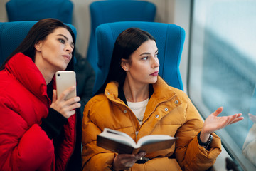 Young females with book and mobile phone in railway train.