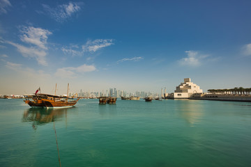 Obraz premium The dhow boats in Doha harbor, neighboring with interesting modern complex of Islamic Art Museum, Qatar