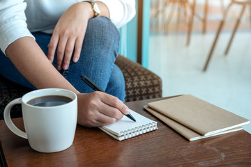 Closeup image of a woman's hand writing on blank notebook with coffee cup on wooden table
