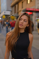 Fototapeta premium Beautiful brunette young woman wearing black shirt and walking on a street of the city watchig shop windows