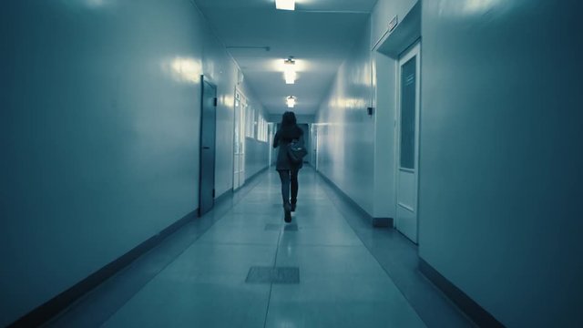 A young excited woman in a panic runs away from her pursuer along a dark corridor. A flickering sign with Russian text above the doors: exit.