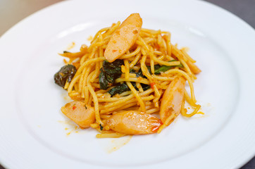 Spaghetti with sausage, Stir-fried sausage, Italian food.Spaghetti with red sauce, white plate on the table in the morning restaurant.