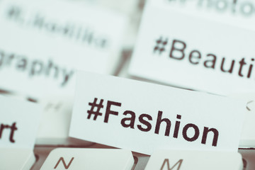 Popular hashtag 'fashion' printed on paper and on the keyboard. Close up. Toned.