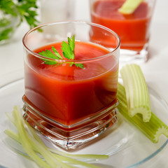 Tomato juice in glass. Tomato juice is poured into a transparent glass with parsley and herring, on a white background, illuminated by sunlight.