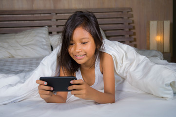 happy and beautiful 7 years old child having fun playing internet game with mobile phone lying on bed cheerful and excited in young girl and technology concept