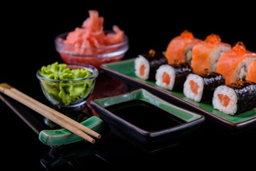 Japanese food. A set of various rolls of salmon, eel, shrimp and red caviar, in a beautiful green bowl, on a black background with reflection.