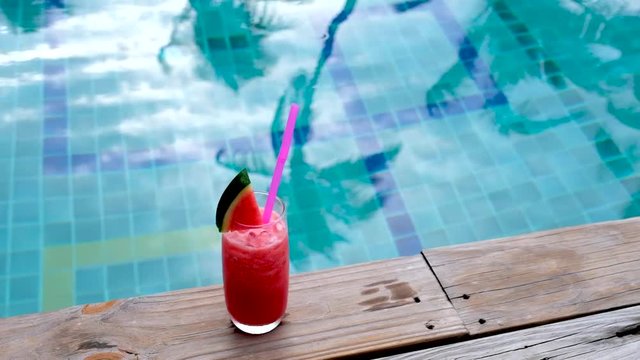 Water melon red fresh juice and Pineapple smoothie drink cocktail near swimming pool. slow motion- wind and coconut leaf shape move in the water