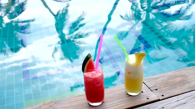 Water melon red fresh juice and Pineapple smoothie drink cocktail near swimming pool. slow motion- wind and coconut leaf shape move in the water