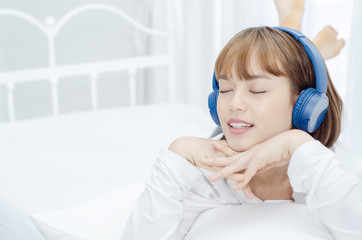 Beautiful woman listening to music on a white bedroom bed.Girl wearing blue headphones.Women wearing white shirts are smiling.