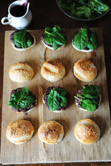 Burger with spinach greens, cutlet, berry sauce and sesame bun. Process of cooking. Layout on a wooden board