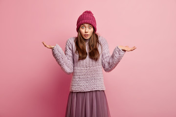 Emotional puzzled uncertain young woman raises palms, makes decision, looks in bewilderment, wears...
