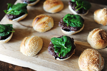 Burger with spinach greens, cutlet, berry sauce and sesame bun. Process of cooking. Layout on a wooden board