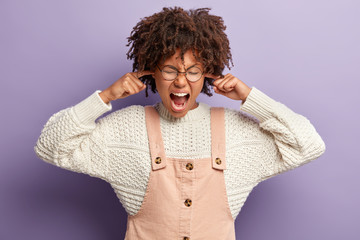 Stressful ethnic woman plugs ears, ignores quarrel during conflict situation, shouts loudly to be...
