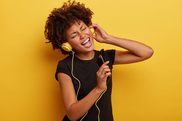 Carefree hipster with Afro haircut feels excited to hear new song, entertains herself with lively...