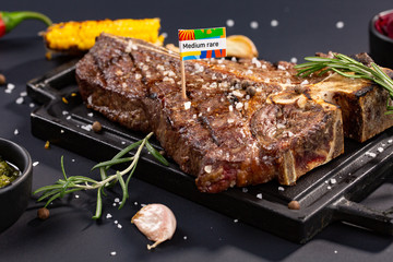 Delicious beef steak on black stone cutting board. Grilled meat served with grilled corn, garlic, rosemary, sauces, chilli and salt. nameplate or checkbox medium rare