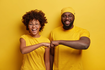 Studio shot of overjoyed satisfied woman and man with dark skin, give fist bump, agree to work...