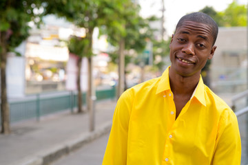 Fototapeta premium Young happy bald African businessman smiling in the city streets outdoors