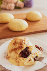 Germknödel oder Hefeklöße mit Pflaumenmusfüllung und Vanillesoße auf weißem Teller und hellem Holzuntergrund