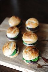 Six freshly cooked burgers on a wooden board. Sesame bun, beef cutlet, spinach greens and berry sauce.