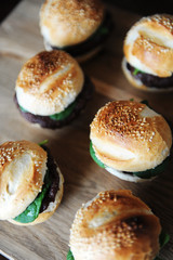 Six freshly cooked burgers on a wooden board. Sesame bun, beef cutlet, spinach greens and berry sauce.