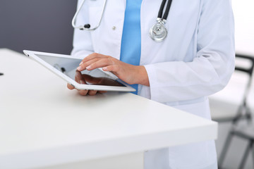 Unknown doctor woman at work. Female physician using digital tablet  while standing near reception desk at clinic or emergency hospital. Medicine and healthcare concept