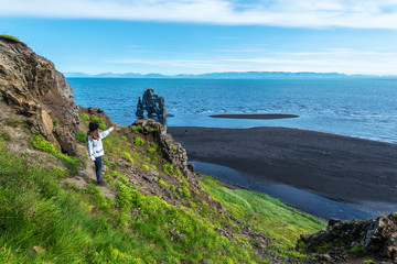 Girl tourist looking at Hvitserkur basalt stack washed with waters of Hindisvik bay in Northwest...