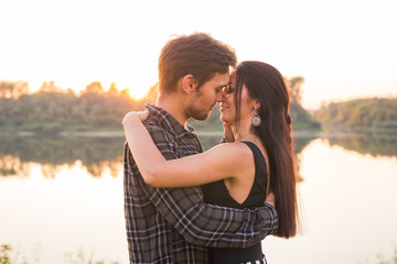 Fototapeta premium Relationship, love and nature concept - Close up portrait of attractive woman and handsome man hugging on the background of the lake