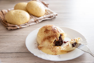 Germknödel oder Hefeklöße mit Pflaumenmusfüllung und Vanillesoße auf weißem Teller und hellem Holzuntergrund