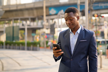 Young handsome African businessman using phone in the city