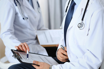 Two unknown doctors filling up medical form on clipboard, just hands closeup. Physicians asking question to patient or discussing medication program. Healthcare, insurance and medicine concept