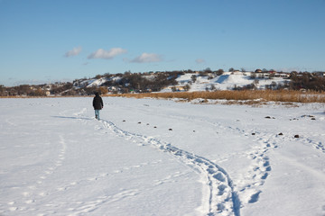 The human goes into the distance, leaving behind traces on the snow. Beautiful snow-covered field, mountain and clouds in the background.