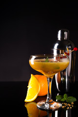 Glass of the orange alcoholic drink with ice and slice of orange peel on the dark background