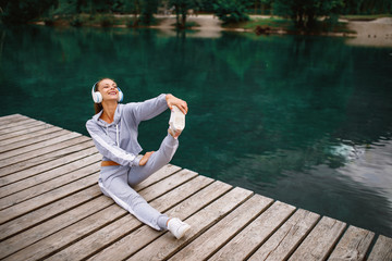 Fototapeta na wymiar Young sports woman stretching legs at dock on the lake in the mountains