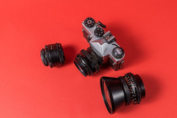 Retro film photo camera and lenses isolated on red background.