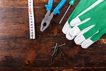 Work gloves and carpenter tools lie on a brown wooden table. view from above. space for text.