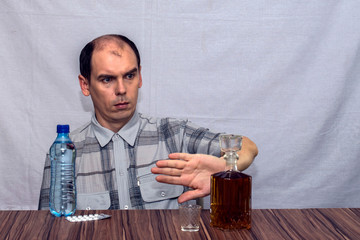 man at the table, next to him a bottle of water and pills. Hands, he fenced off from the bottle with alcohol.