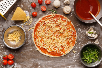 Unbaked pizza with grated cheese and with ingredients around