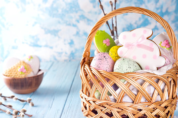 Colorful easter eggs and glazed cookies in basket on blue wooden background