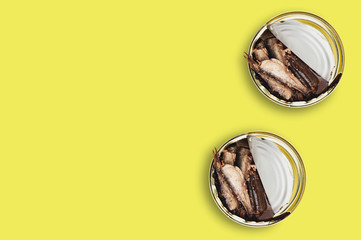 Two open metal cans with preserved fish in oil on yellow table on cuisine. Copy space for your text. Top view. Fast food or cooking concept