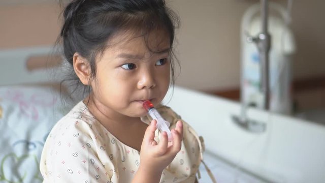 Asian child cute or kid girl Influenza sick holding and eating or taking sweet red drug or water medicine by syringe pump on bed at hospital room for pediatric patient treatment and healthcare on slow
