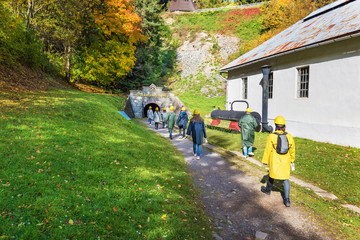 Group of visitors dressed in a mining mantel, with a helmet and a lantern walk into mine shaft