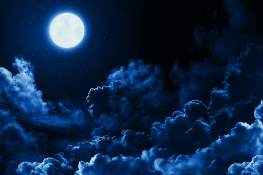 Mystical bright full moon in the midnight sky with stars surrounded by dramatic clouds. Dark natural background with twilight night sky with moon and clouds