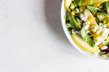 Mix salad with corn, apple, avocado and fresh farm cottage cheese. Healthy and diet food concept. Light concrete background. Copy space.