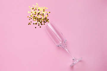 Champagne glass with golden confetti on pink color paper background minimal style