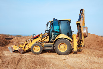 Excavator loader working at ground area on blue sky background, digging process. Yellow bucket. Outdoors, copy space.