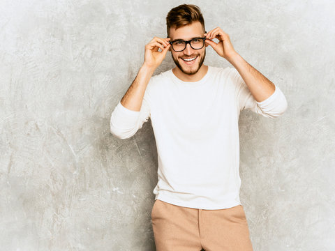 Portrait of handsome smiling hipster lumbersexual businessman model wearing casual summer white clothes and spectacles. Fashion stylish man posing against gray wall