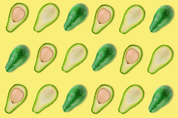 Rows of whole and halves of organic avocado with and without kernels in center of yellow table in kitchen or market. Top view. Cooking concept. Seamless pattern