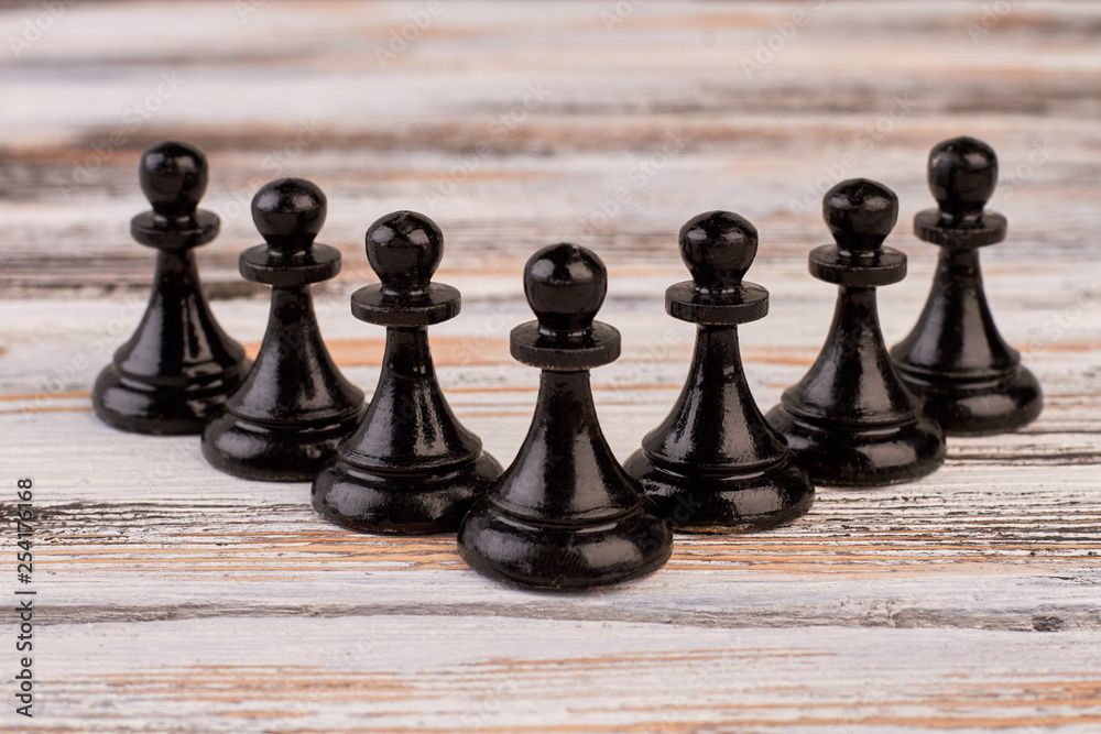 Wall mural Composition of black chess pawns. Set of black chess pieces on light wooden background. Playing chess for intellectual development.